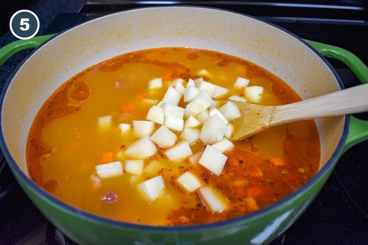 Diced potatoes being stirred into the simmering soup.