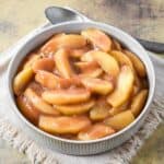 Cinnamon apples served in a round bowl, coated in a glossy brown sugar and cinnamon sauce.
