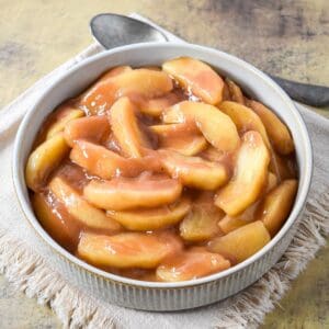 Cinnamon apples served in a round bowl, coated in a glossy brown sugar and cinnamon sauce.