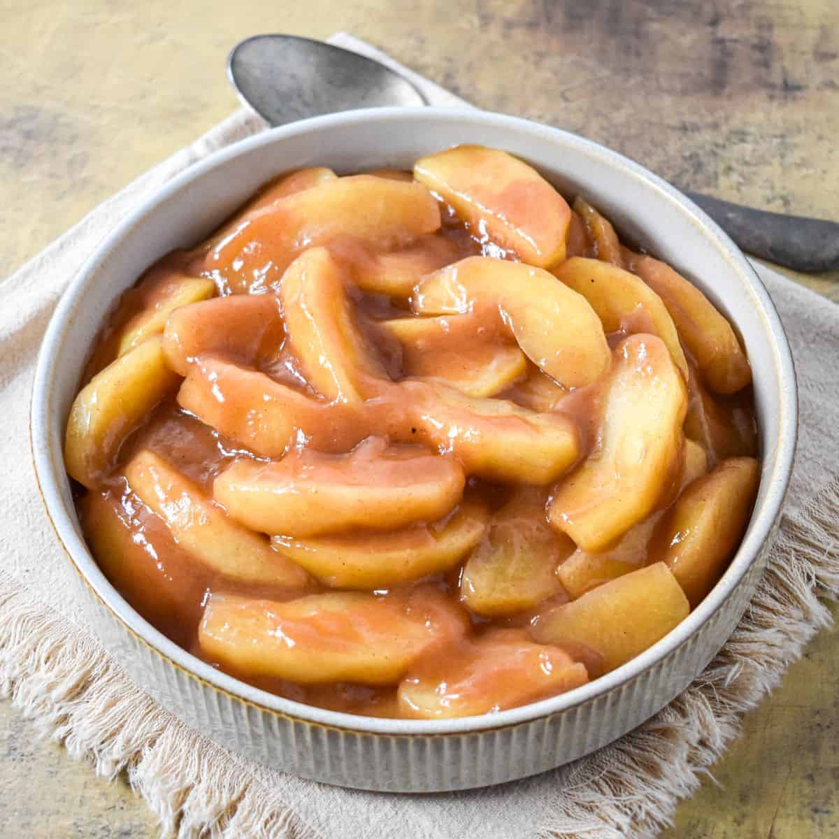 Cinnamon apples served in a round bowl, coated in a glossy brown sugar and cinnamon sauce.