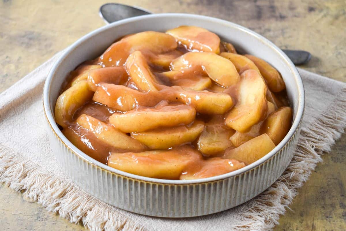 Overhead view of cooked apples in a spiced brown sugar glaze, served in a bowl with a spoon beside it.