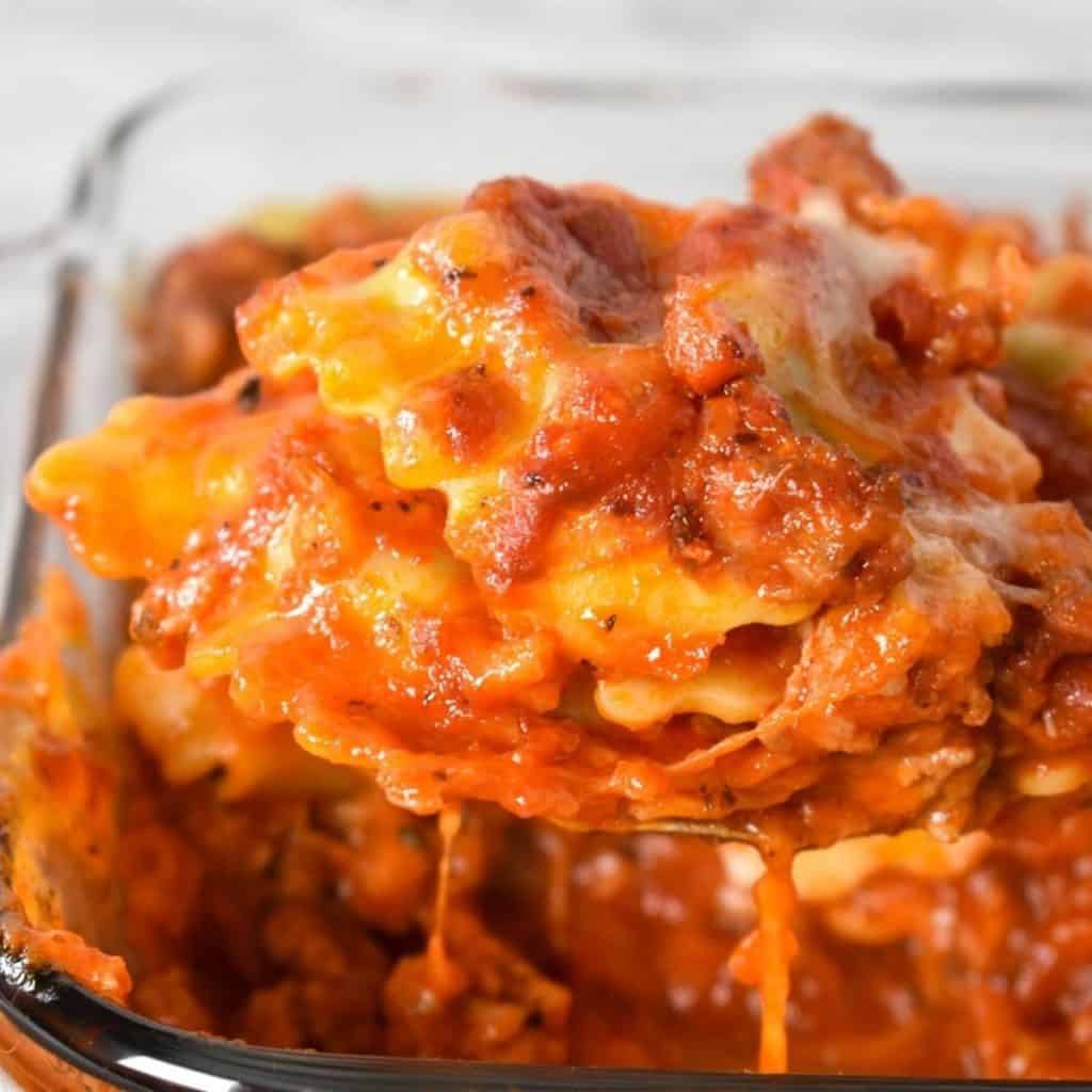 Ravioli bake being lifted by a large spoon from a glass casserole dish.