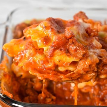 Ravioli bake being lifted by a large spoon from a glass casserole dish.