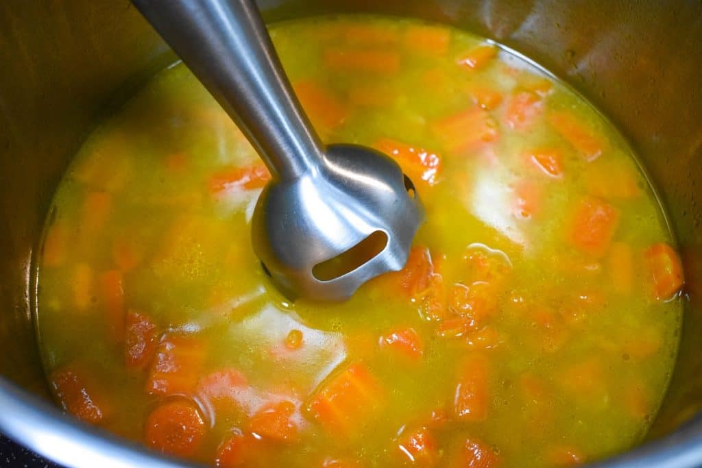 An immersion blender going into the pot of carrot soup.