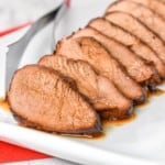 Asian marinated pork tenderloin sliced into thin pieces and served on a white platter.