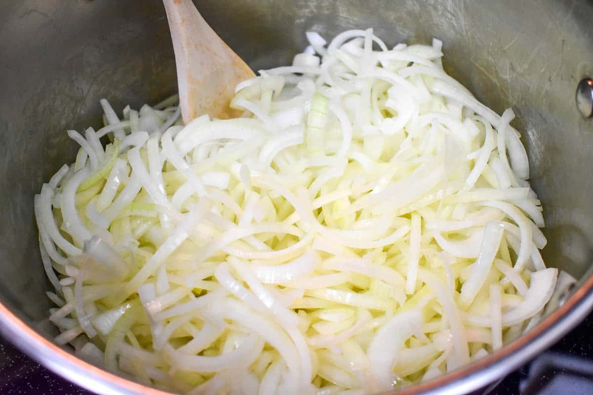 Sliced onions in a large pot with a wooden spoon.