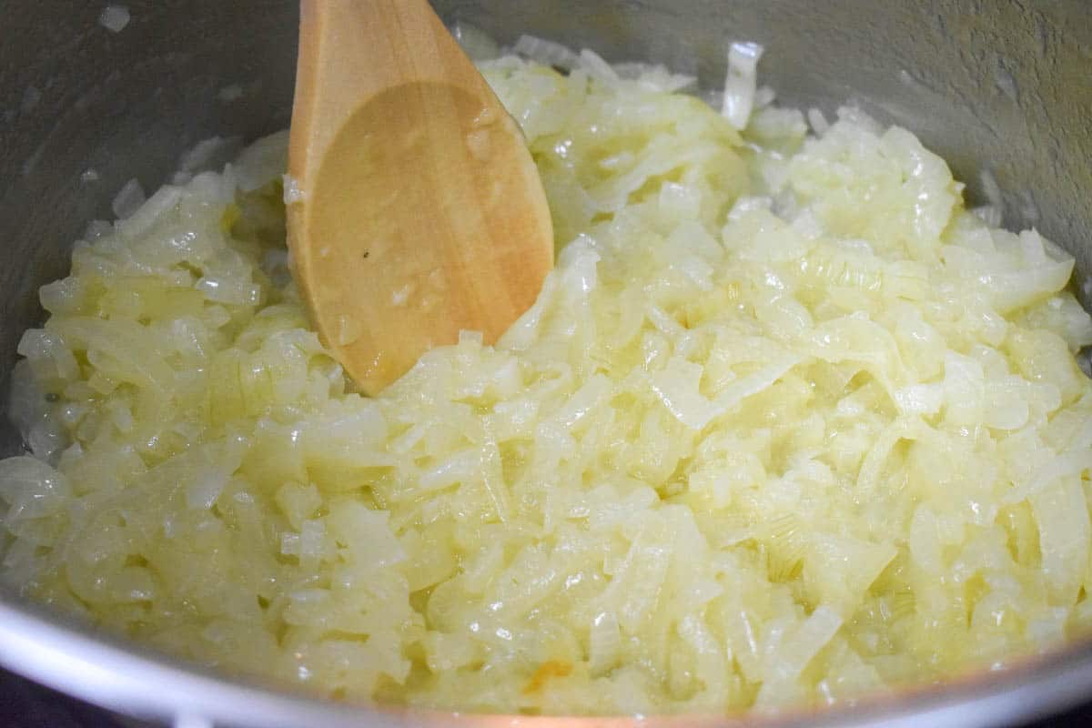 An image of the sliced onions, further reduced and softened in a large pot with a wooden spoon.