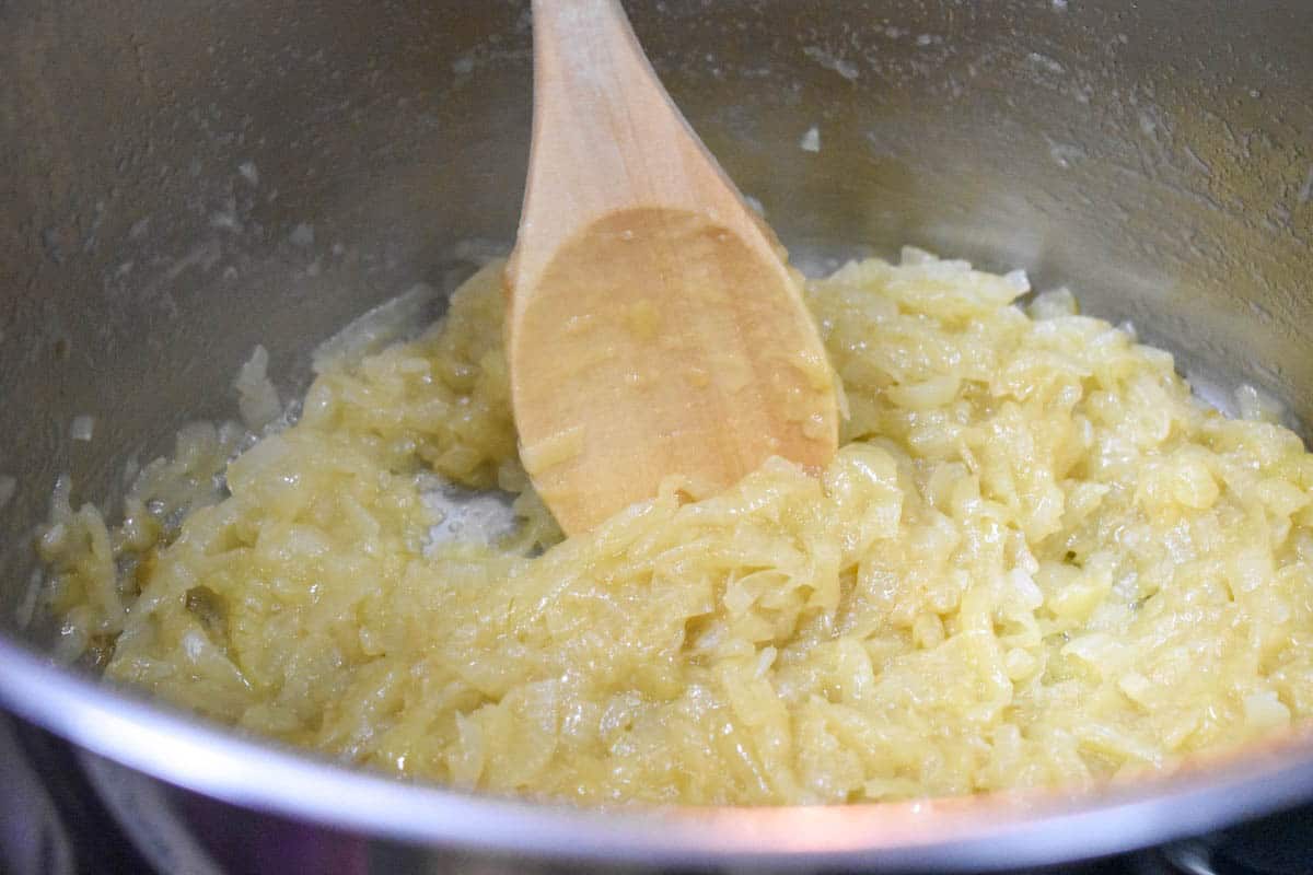 An image of the sliced onions starting to turn a soft golden color, in a large pot with a wooden spoon.