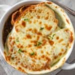 The French onion soup served in a white bowl and set on a beige linen.