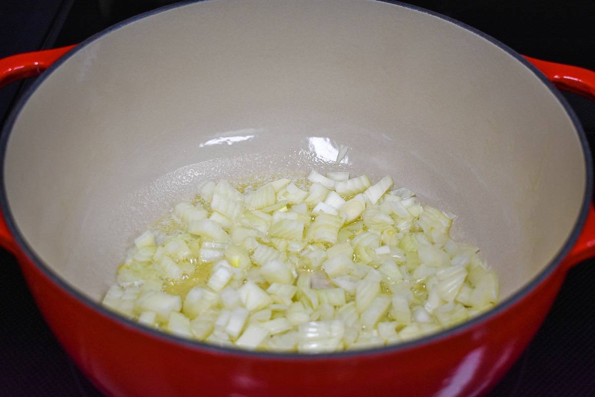 Diced onions cooking in a large red and white pot.