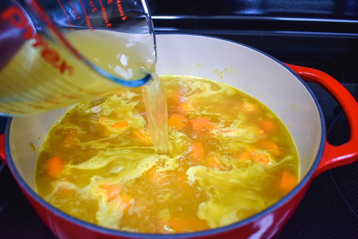 Chicken broth being added to the carrots and onion mixture in the pot.