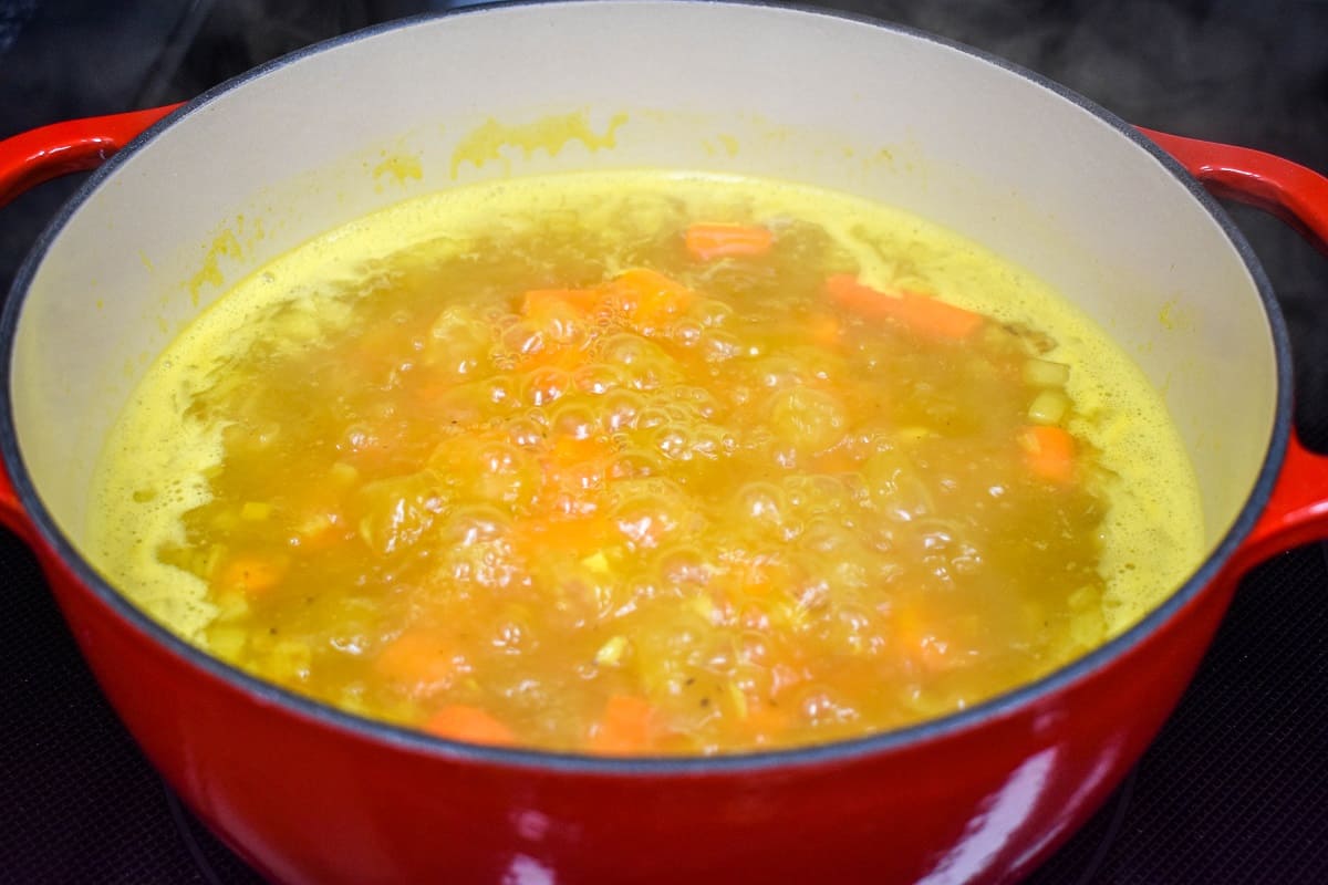 The carrot soup simmering in a white and red pot.