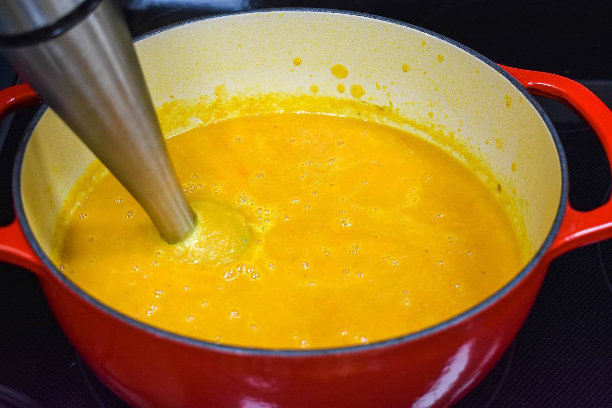 The soup being processed in the pot with an immersion blender.