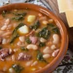 Cuban white bean soup served in a terracotta bowl with sliced bread on the side.