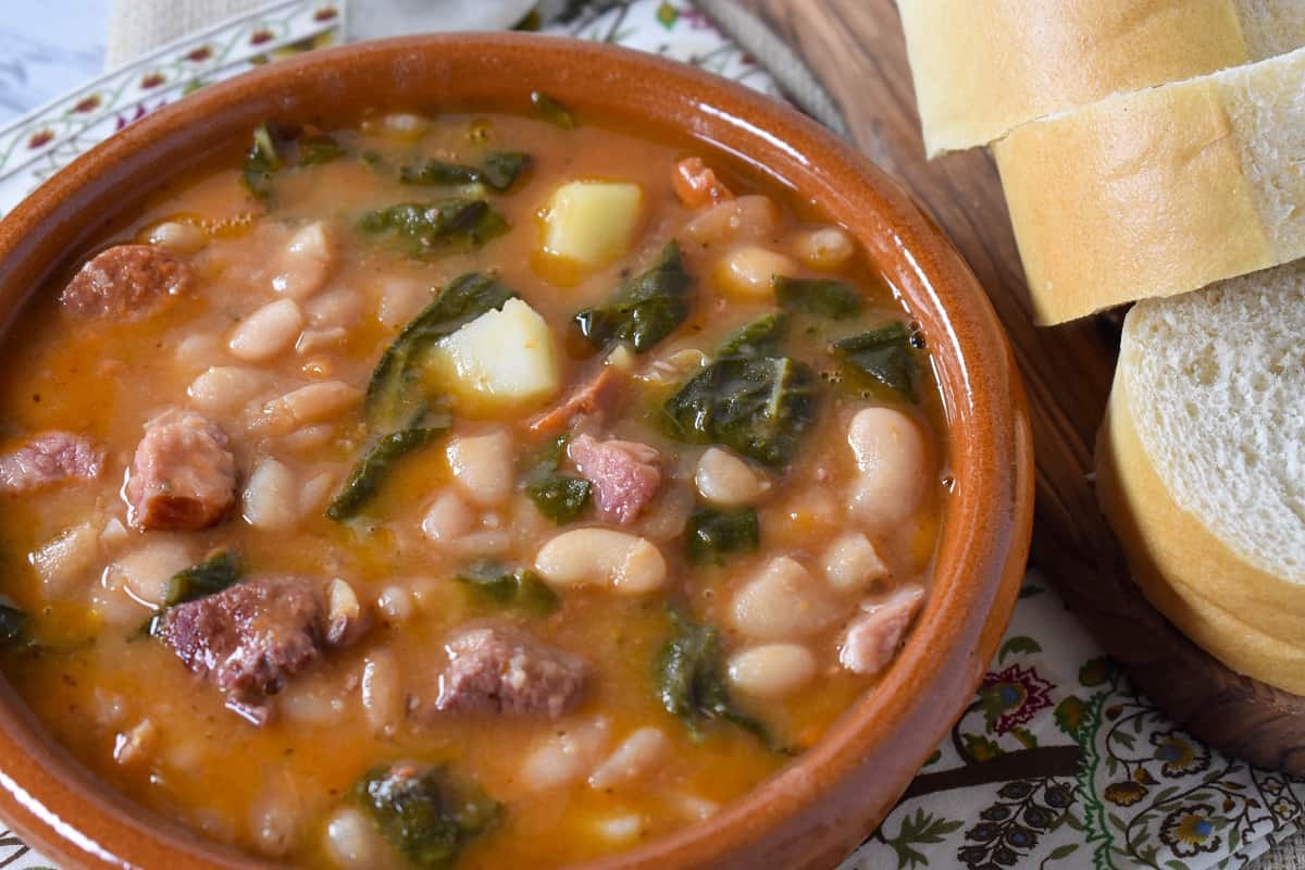 Cuban white bean soup served in a terracotta bowl with sliced bread on the side.