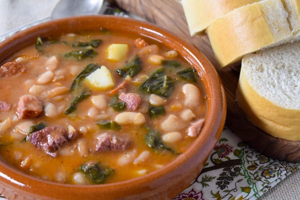 Cuban white bean soup served in a terracotta bowl with sliced bread on the side.