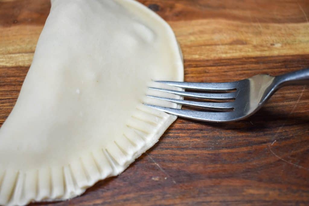 An image of a fork crimping the edge of the folded empanada.