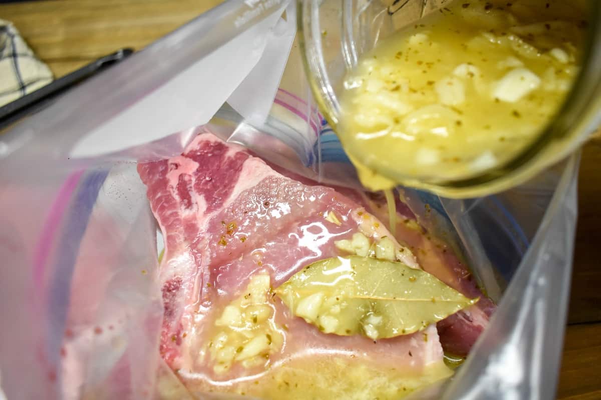 Pouring Mojo Marinade on pork chops that are in a plastic bag.