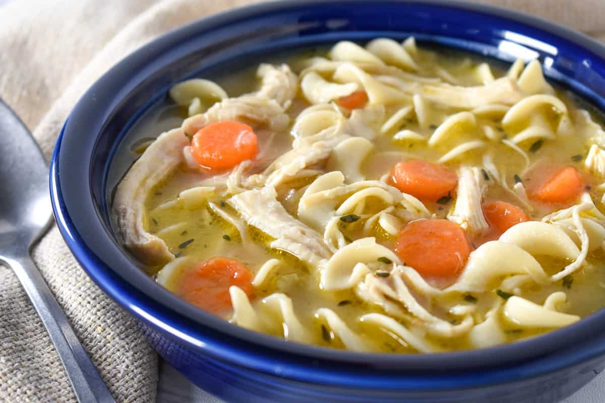 A close up image of chicken egg noodle soup served in a blue bowl.