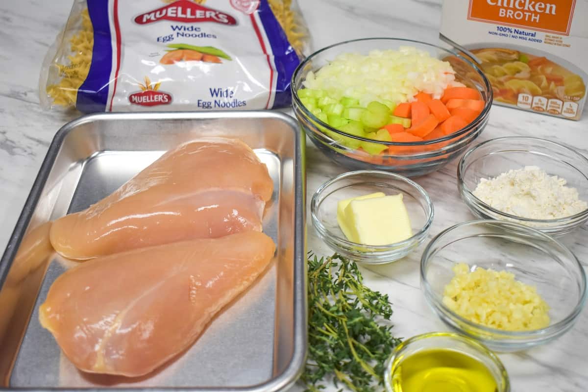 The prepped ingredients for the chicken and egg noodle soup displayed on a white table.