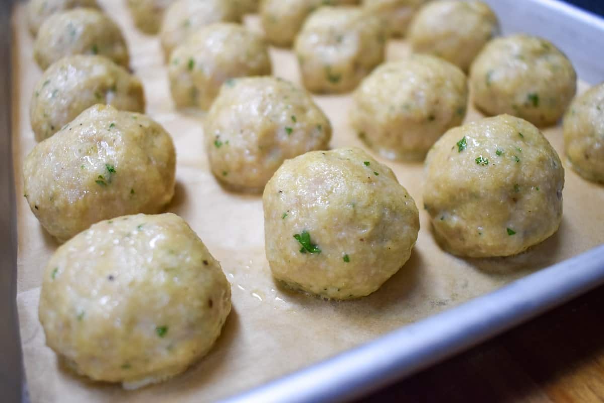 Cooked chicken meatballs arranged on a baking sheet lined with parchment paper. 