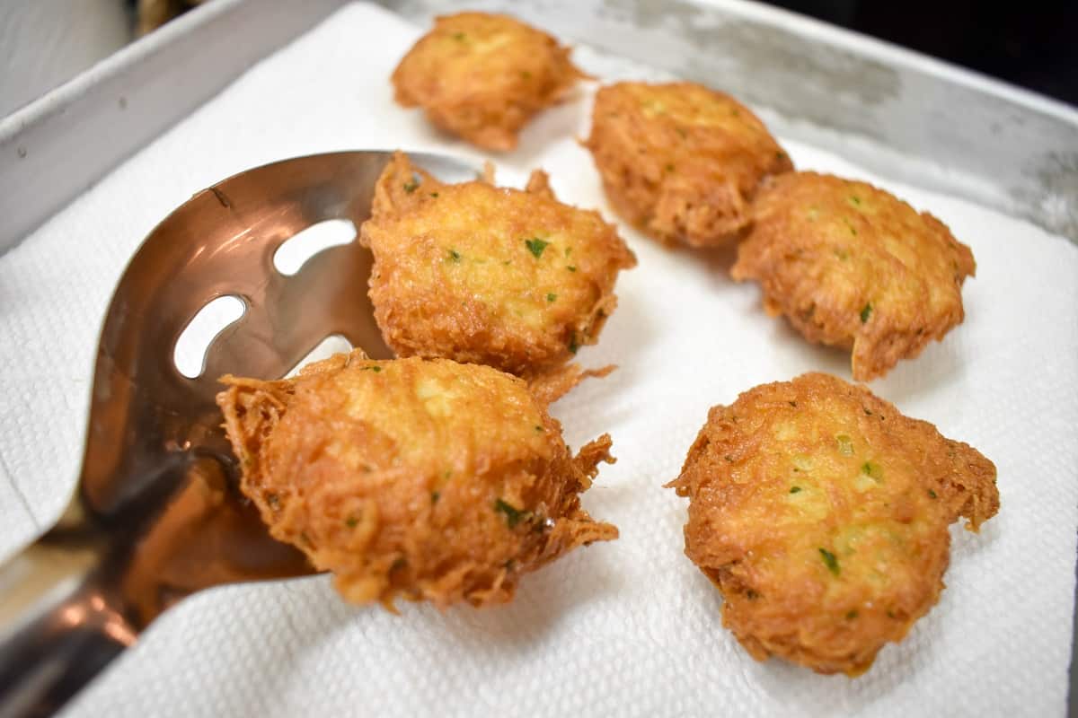 Malanga fritters being placed by a slotted spoon on a paper towel lined pan to drain.