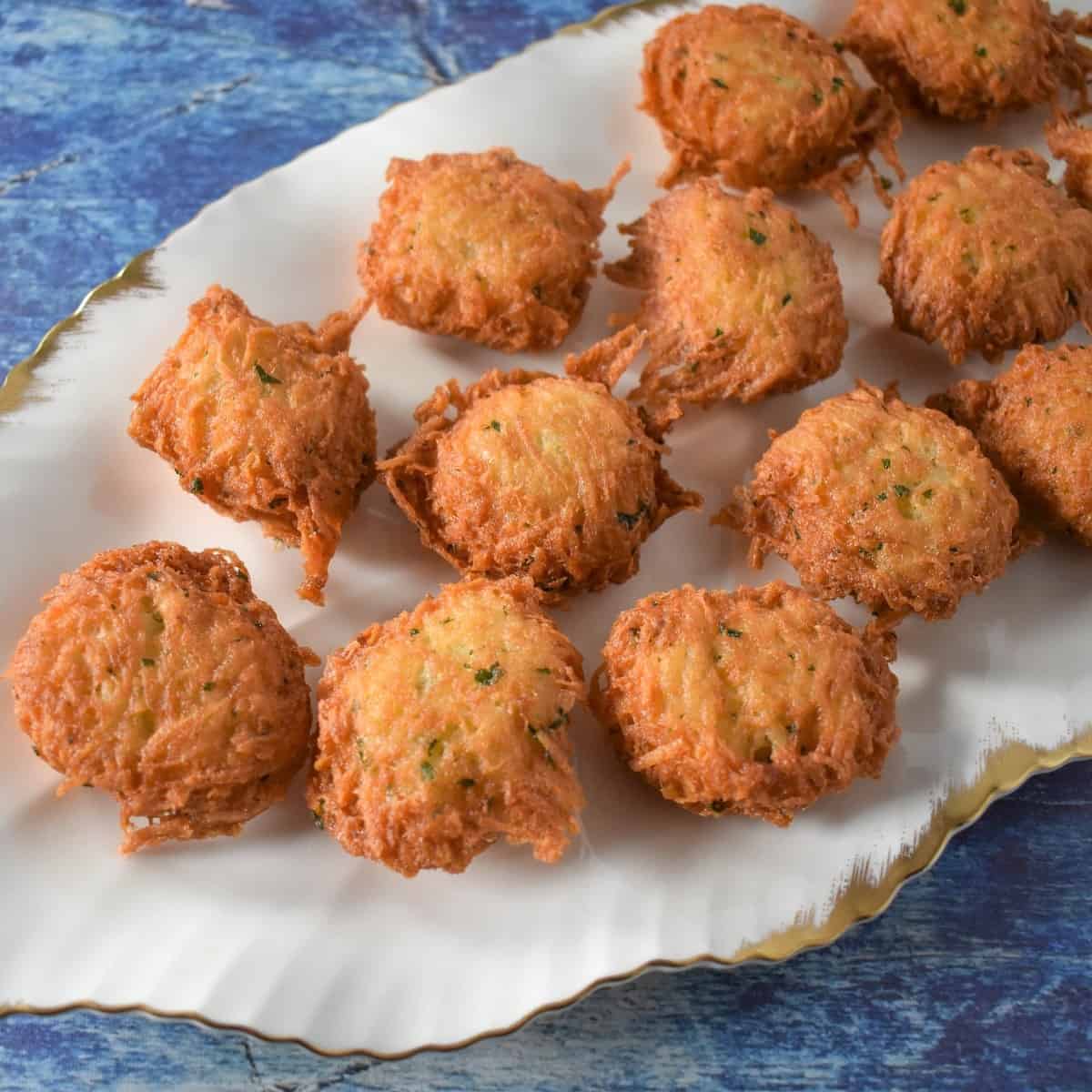 Malanga fritters arranged on a white platter set on a blue table.