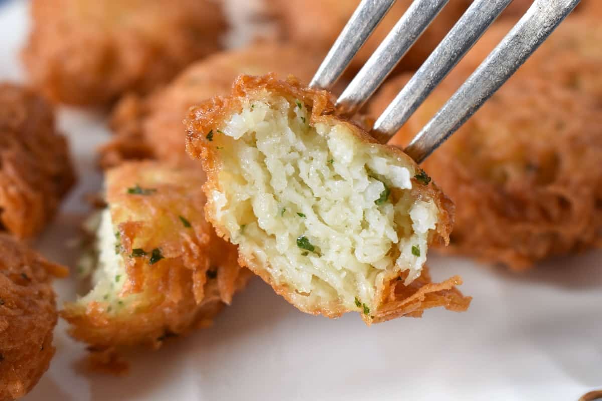 A malanga fritter cut in half, the inside being displayed held by a fork.