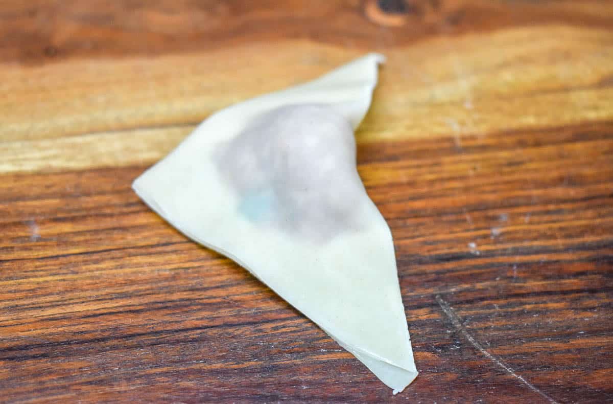 An image of a stuffed wonton wrapper folded in half on a wood cutting board.