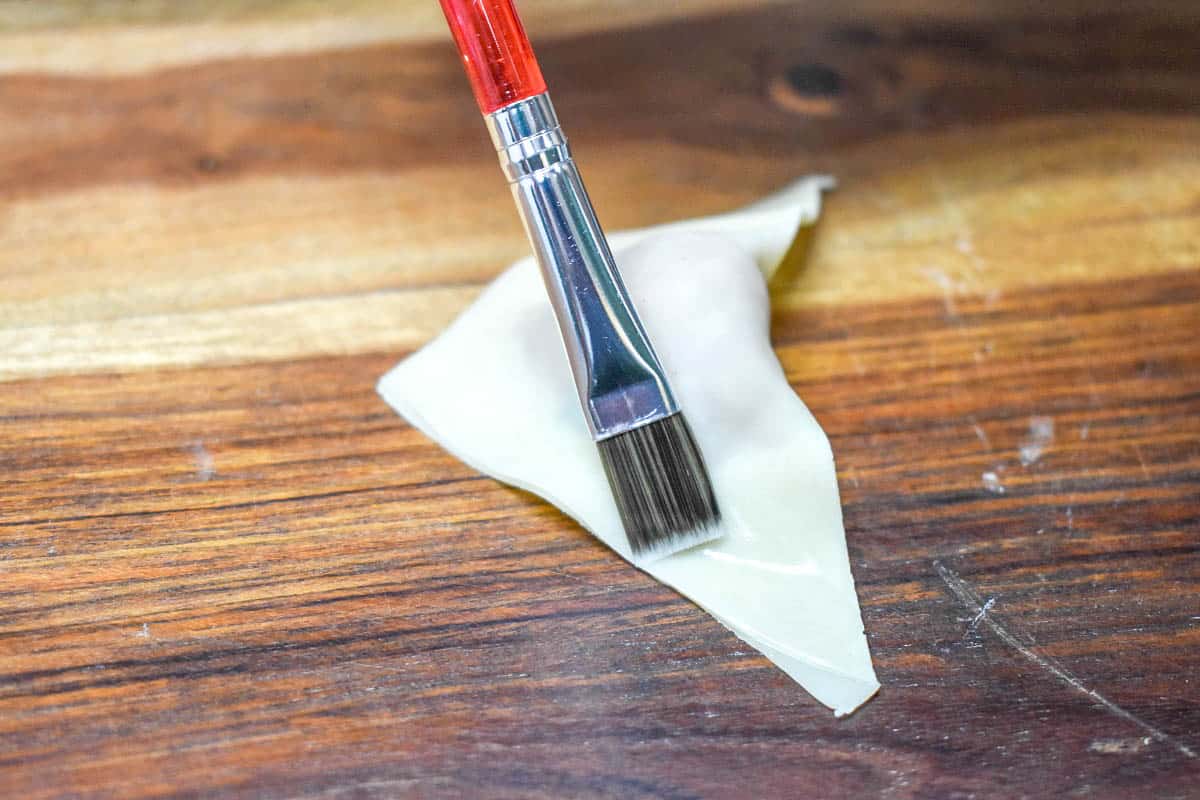 An image of a small pastry brush brushing water on the edge of a folded wonton wrapper.