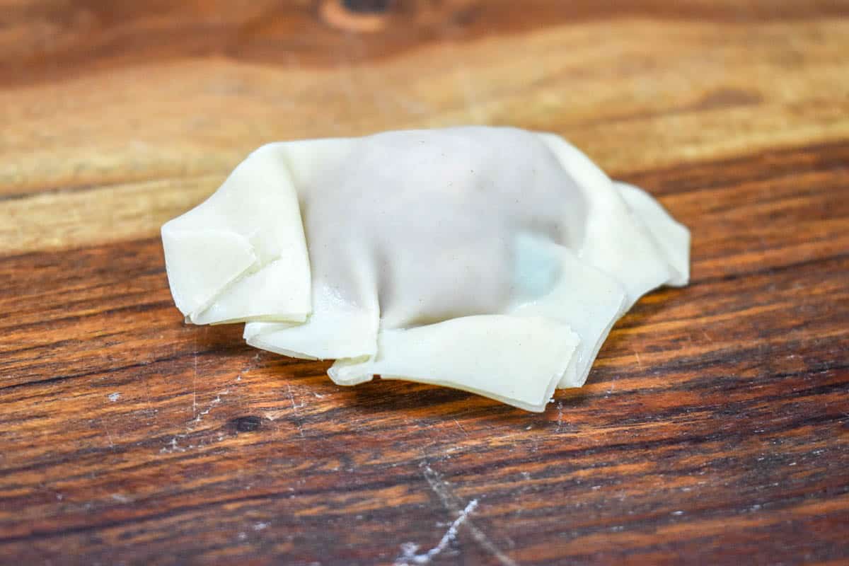 An image of an uncooked potsticker set on a wood cutting board.