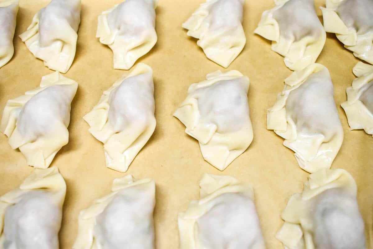 An image of uncooked potstickers set in neat rows on a baking sheet.