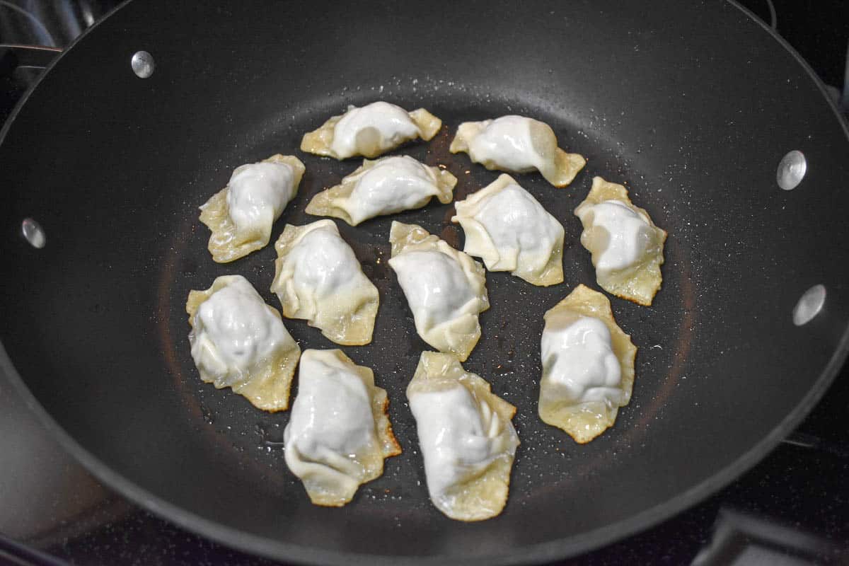 Twelve potstickers in a large, black skillet.