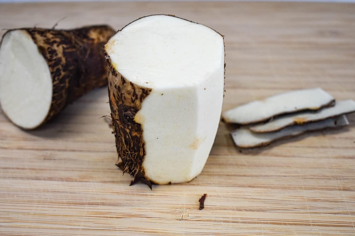 A half peeled malanga on a wood cutting board.