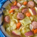 Cabbage sausage soup served in a beige and black bowl set on a blue cloth napkin.