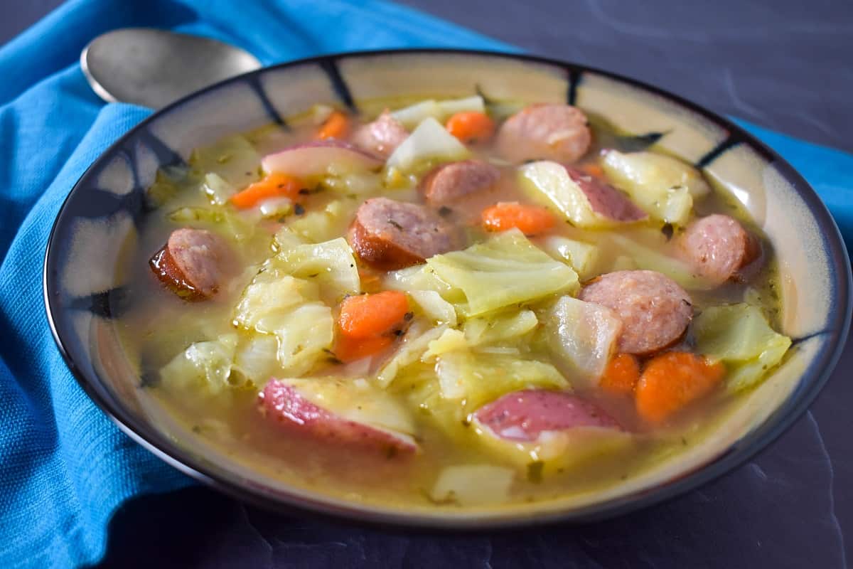 Cabbage sausage soup served in a beige and black bowl.