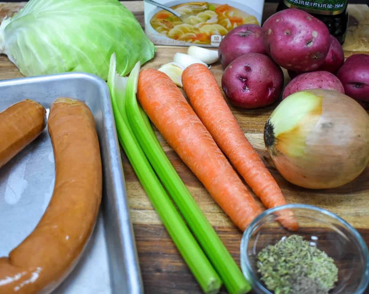 The ingredients for the cabbage sausage soup displayed on a wood cutting board.
