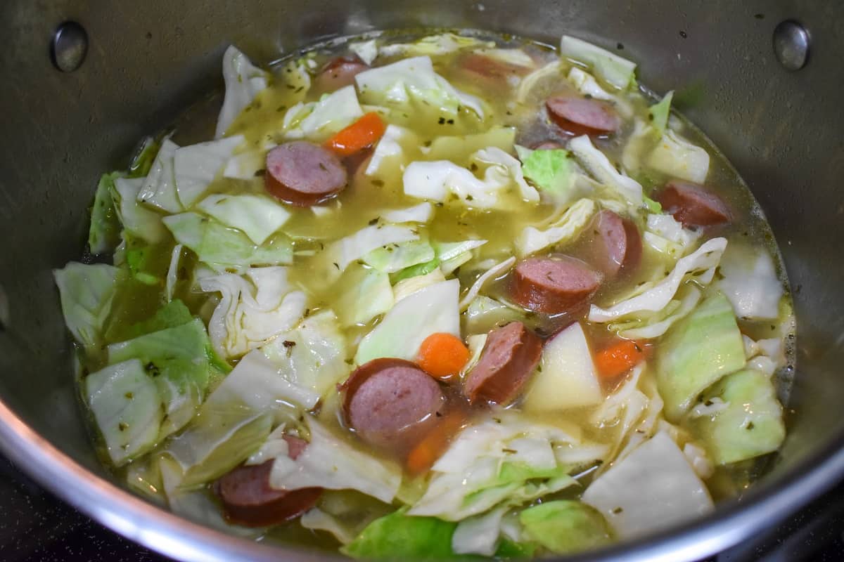 The cabbage sausage soup in a large stainless steel pot.