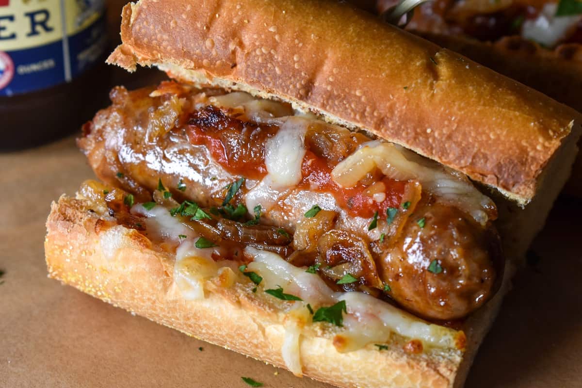 A close up image of an Italian sausage sandwich, served on a wood cutting board lined with brown parchment paper.