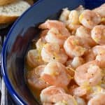 Lemon pepper shrimp served in a blue bowl with small forks on the side and toasted bread rounds in the background.