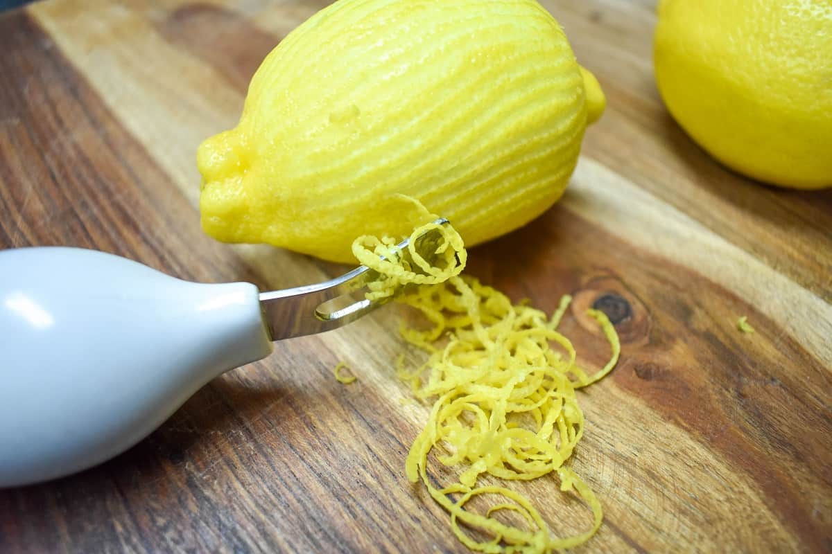 A zested lemon and a zester on a wood cutting board.