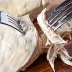 Poached chicken on a cutting board being shredded using two forks.