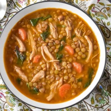 Chicken lentil soup in a white bowl on a light colored flowered linen.