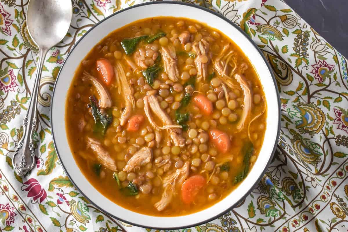 Chicken lentil soup in a white bowl on a light colored flowered linen.