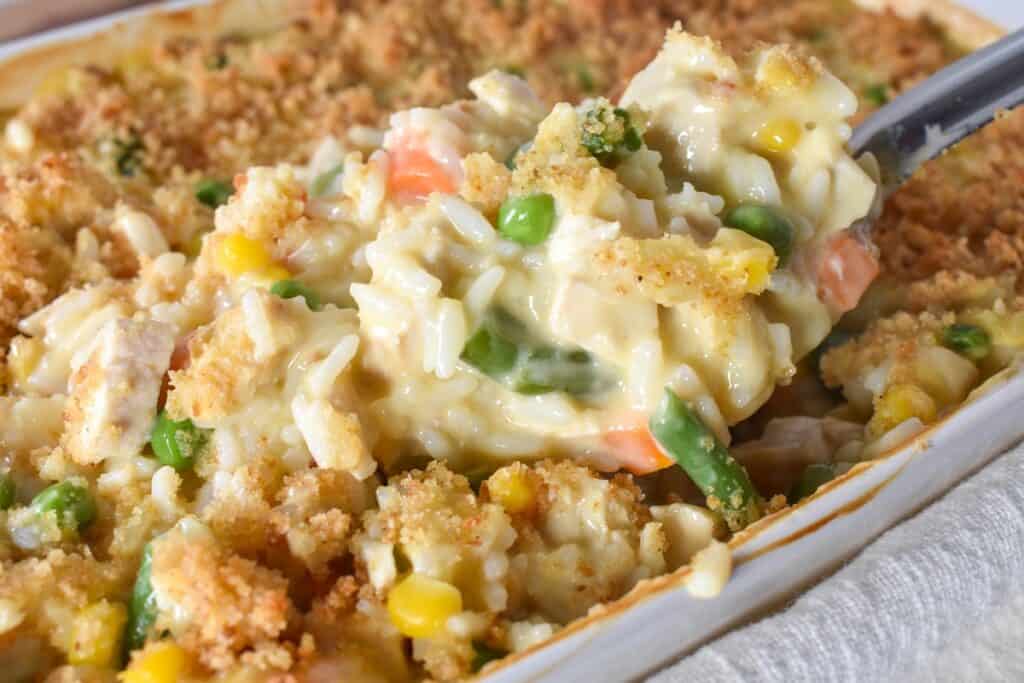 A serving spoon lifting some of the chicken and rice out of the casserole dish.