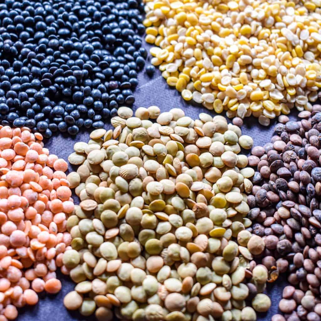 Five different varieties and color of lentils in small piles on black table.