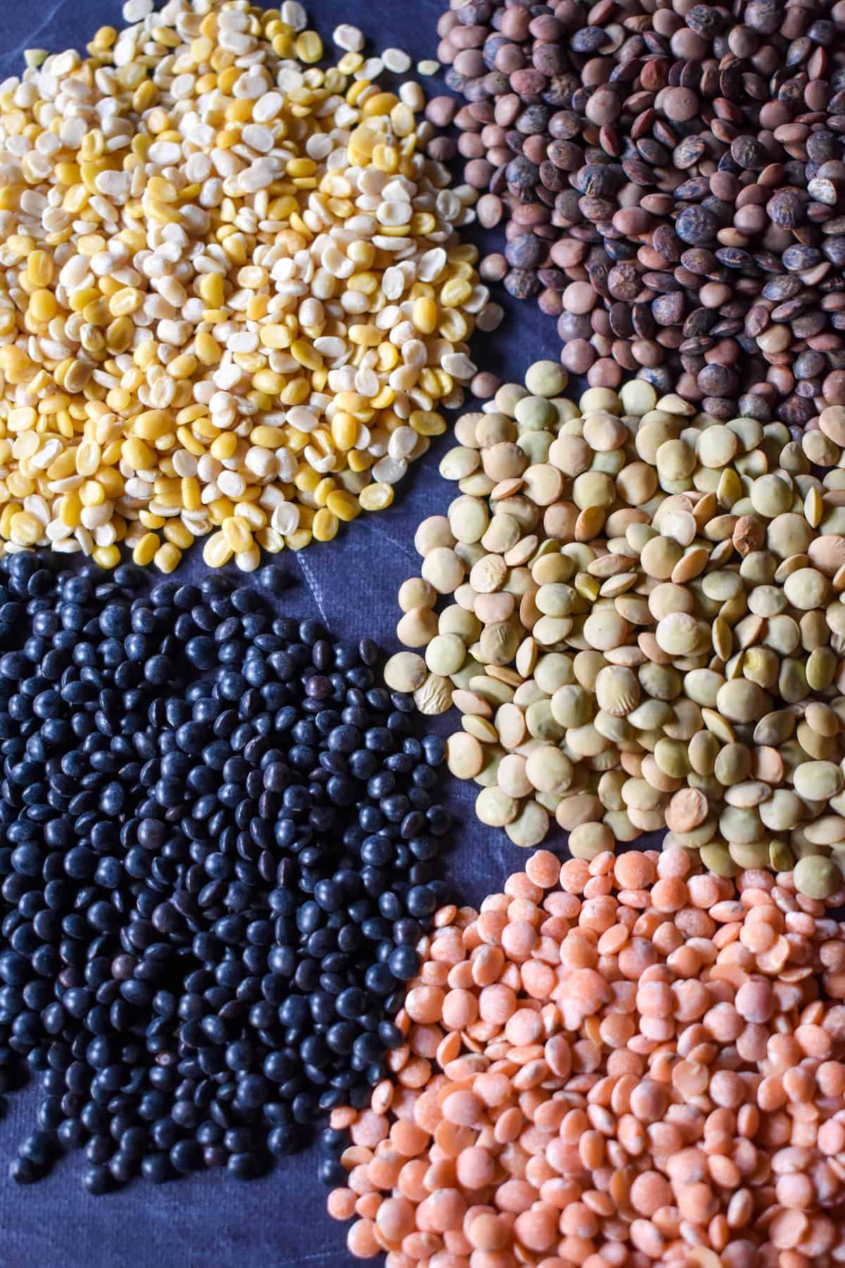 An image of the different lentils arranged in small piles on a black surface.