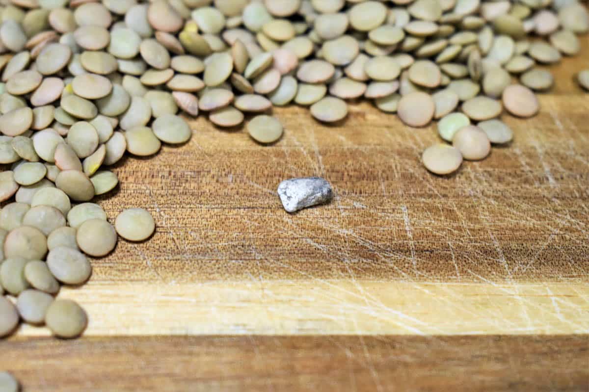 Image of dry lentils on a wood cutting board and a small stone that was found in the lentils.