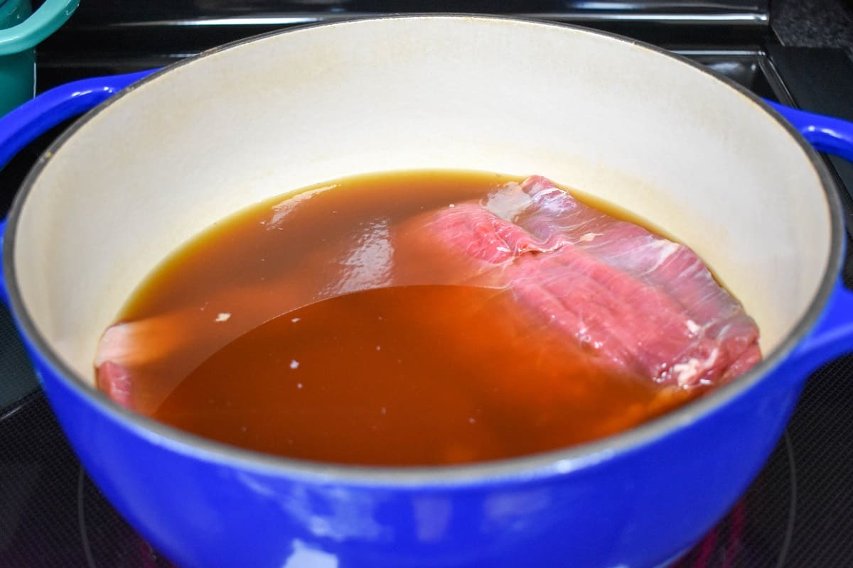 Flank steak covered with beef broth in a blue and white pot.