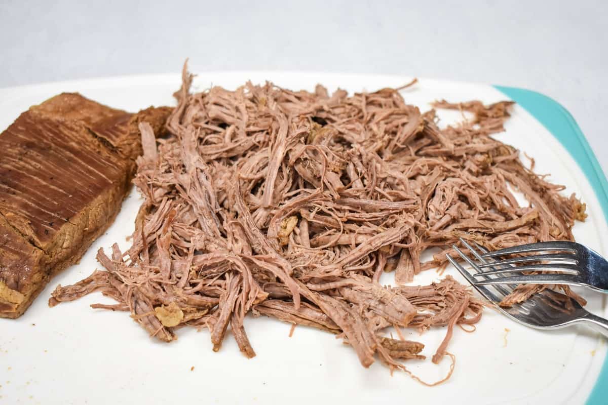 Shredded flank steak on a white cutting board.